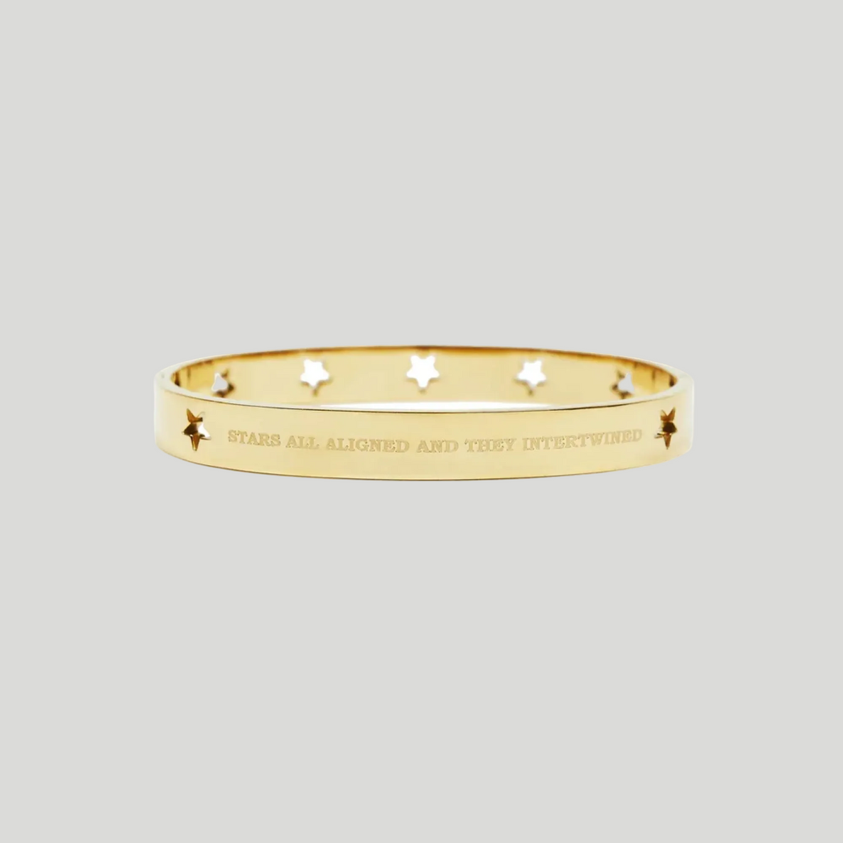 A gold bangle bracelet with star cutouts and the engraved text 'STARS ALL ALIGNED AND THEY INTERTWINED', shown on a plain white background.