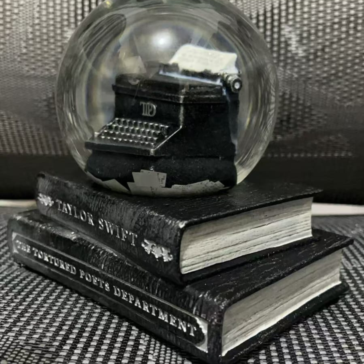 Glass snow globe with a typewriter inside, placed on top of two books.